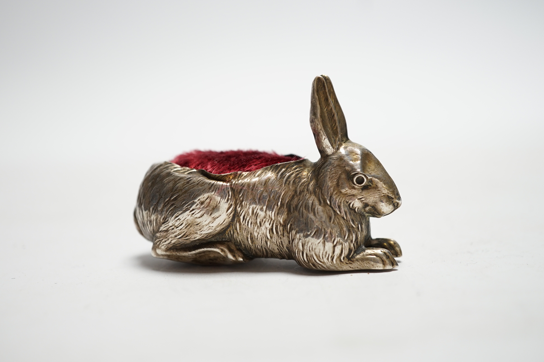 An Edwardian novelty silver mounted pin cushion, modelled as a recumbent rabbit, Henry Matthews, Birmingham, 1907, 64mm.